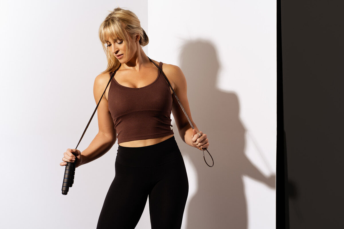 Personal trainer branding photo holding a jump rope and looking down, captured in a studio setting.