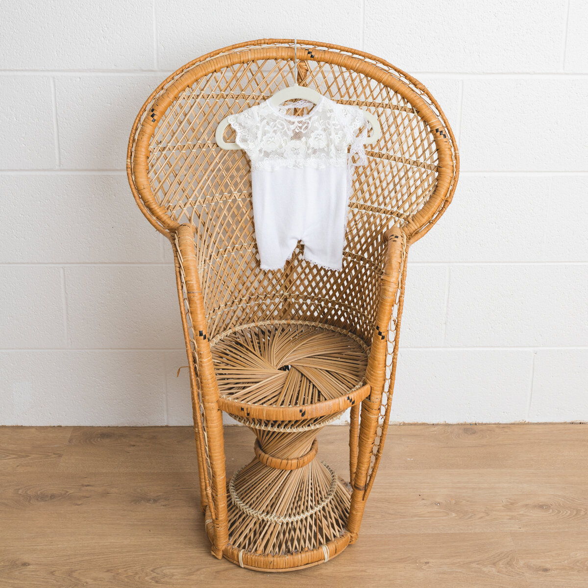 Image depicts a miniature peacock chair in a photography studio on the chair hangs a tiny newborn outfit in white knit  with l a lace bodice.  This image is a sample of Lauren Vanier Photography's newborn client wardrobe. Image taken in Hobart Tasmania