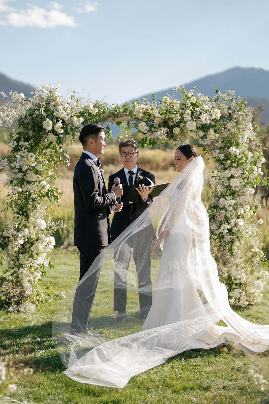The bride and groom share their wedding vows before a white flower altar at their Aspen Meadows Resort wedding ceremony.