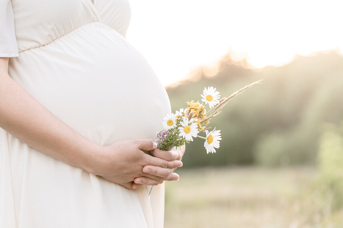 Close up profile of pregnant woman's belly. She is holding belly with some daisies in her hand. Portland Maternity Photographer