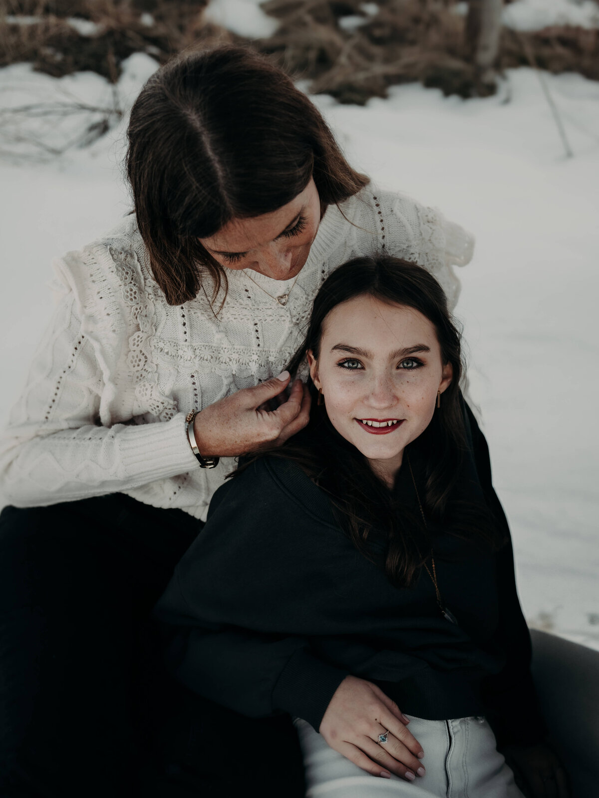 A gorgeous brunette mother, wearing a white sweater brushes through her teenage daughter's hair as she looked up at the camera with her bright blue eyes and a beautiful red lips.