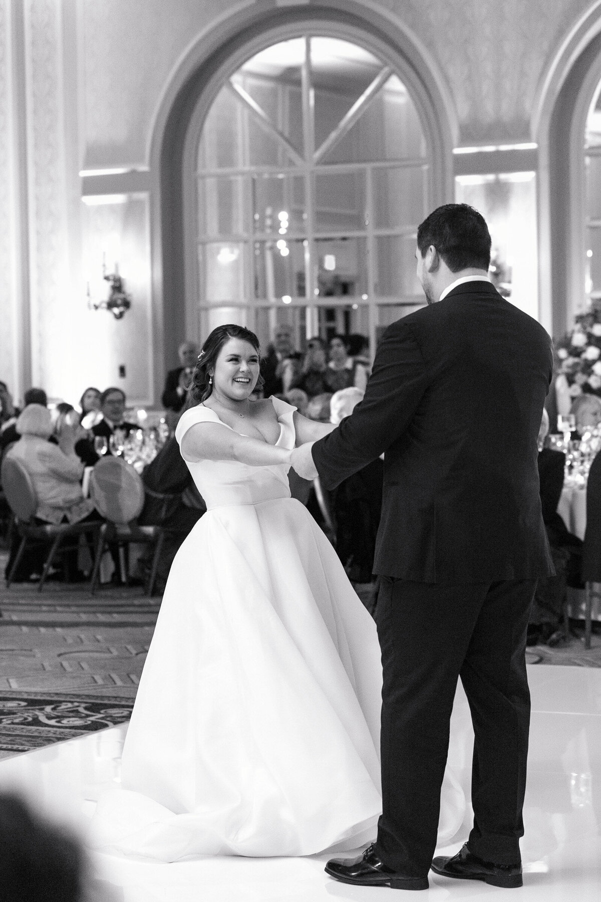 black and white photo of bride and groom during their first dance elegantly styled wedding reception table at The Adolphus in Dallas featuring a black tablecloth, tall glass vases with pink rose arrangements, numerous candles, and refined glassware and chargers