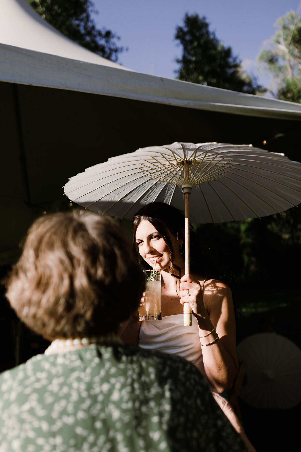 Bride holding sunshade whilst chatting to guests