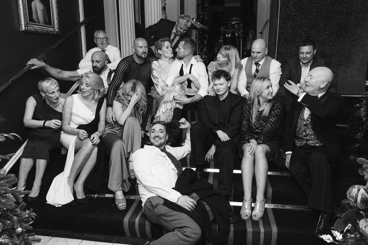 A group photo of wedding guests, sat and laying down across the steps in Prestonfield House