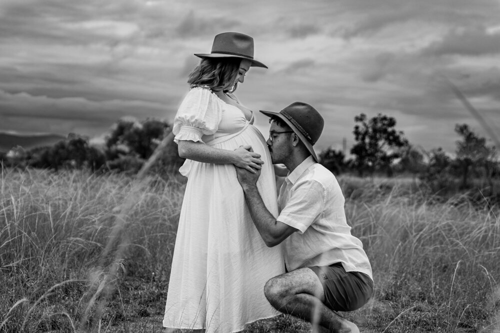 man kissing pregnant partners baby belly in a paddock - Townsville Maternity Photography by Jamie Simmons