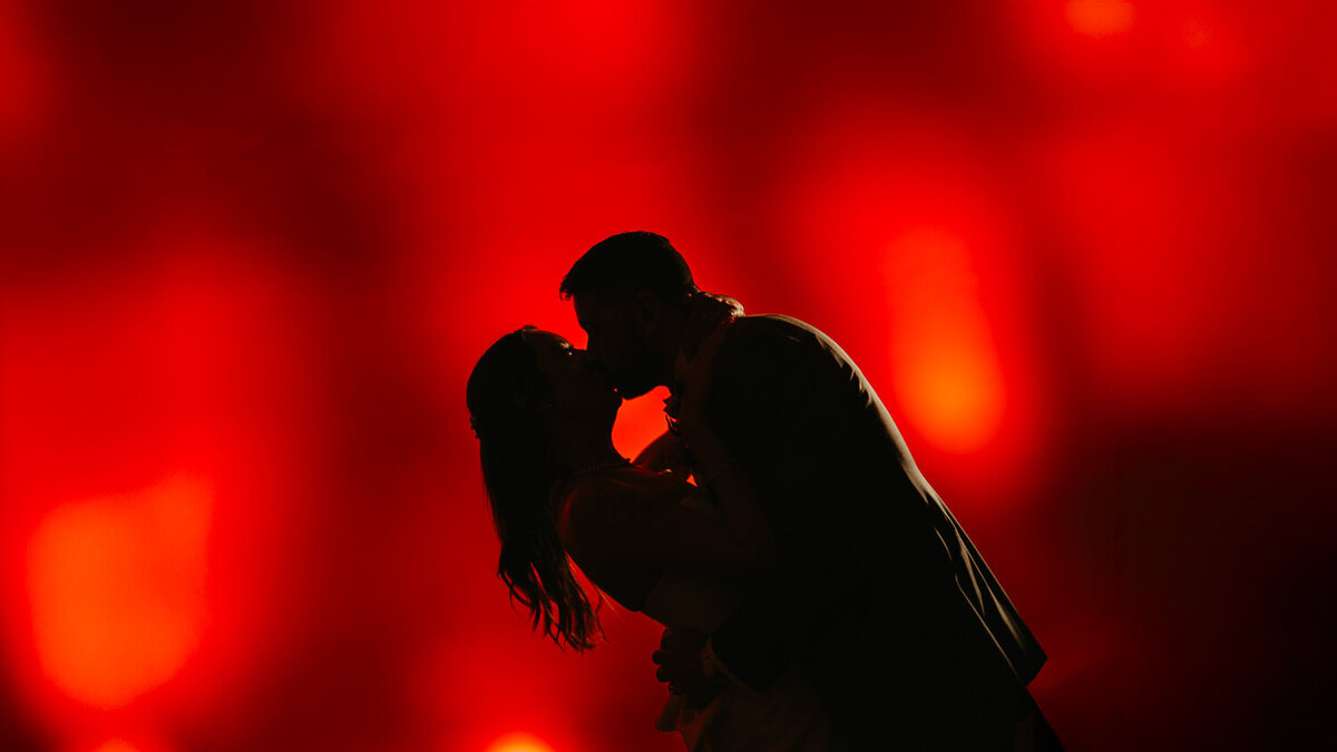 A bride and groom kiss in front of a red screen at Shoreditch Studios. 
