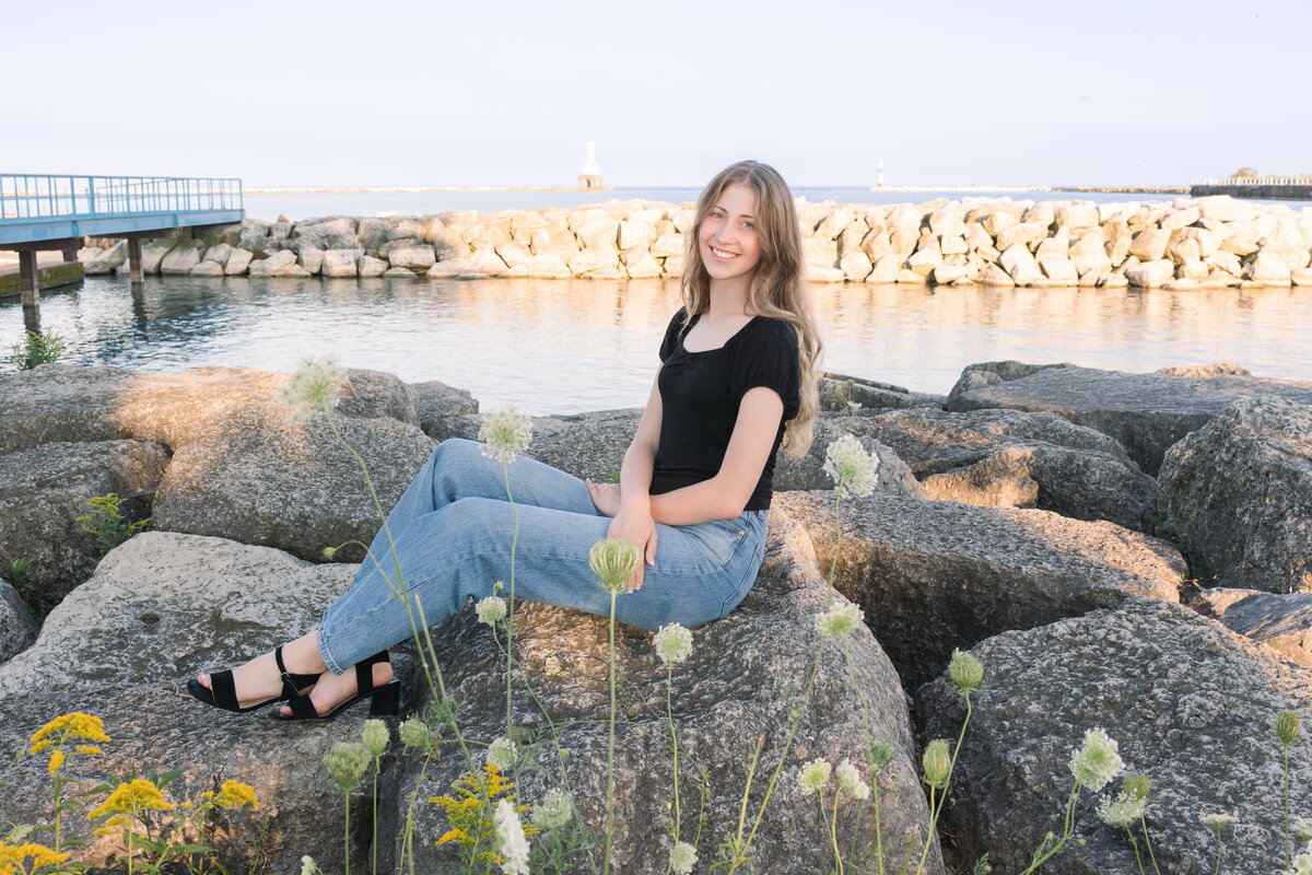 Senior girl seated on rocks next to Lake Michigan smiling at the camera