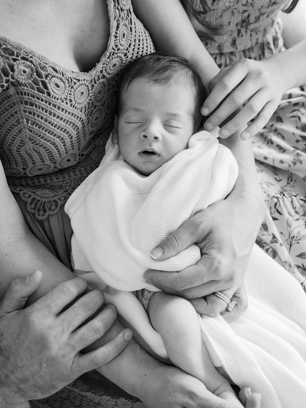 A close-up of a sleeping baby wrapped in a blanket and held in the arms of family during a newborn photography session in Richmond by Katie Stansfield Photography.
