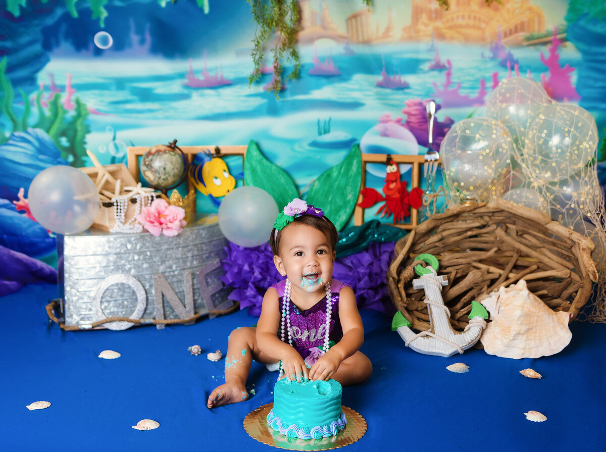 Cake Smash Photographer, a baby girl sits with cake before "Little Mermaid" themed party