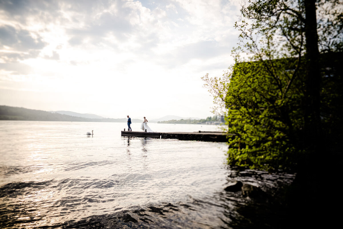 A wedding couples walking down a jetty as a swam head towards them in a moment of serenity