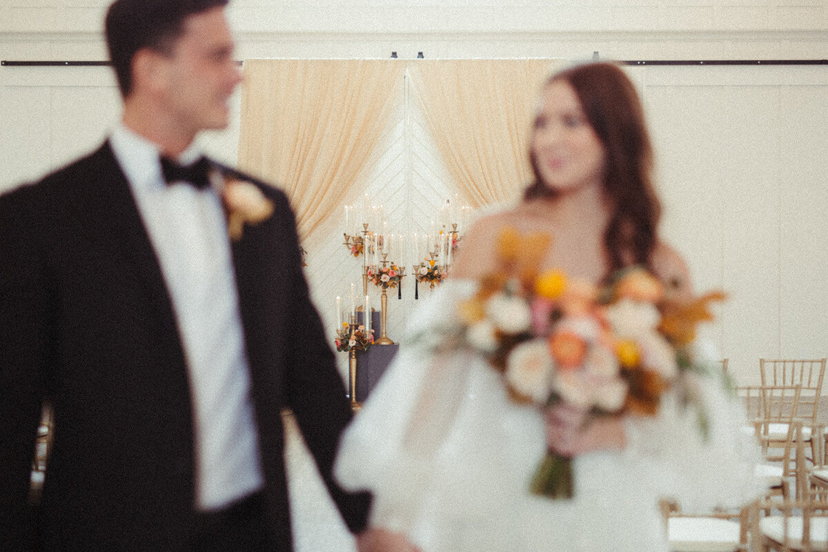 Blurred image of bride and groom wearing a black tuxedo and white wedding gown holding a bouquet of flowers.