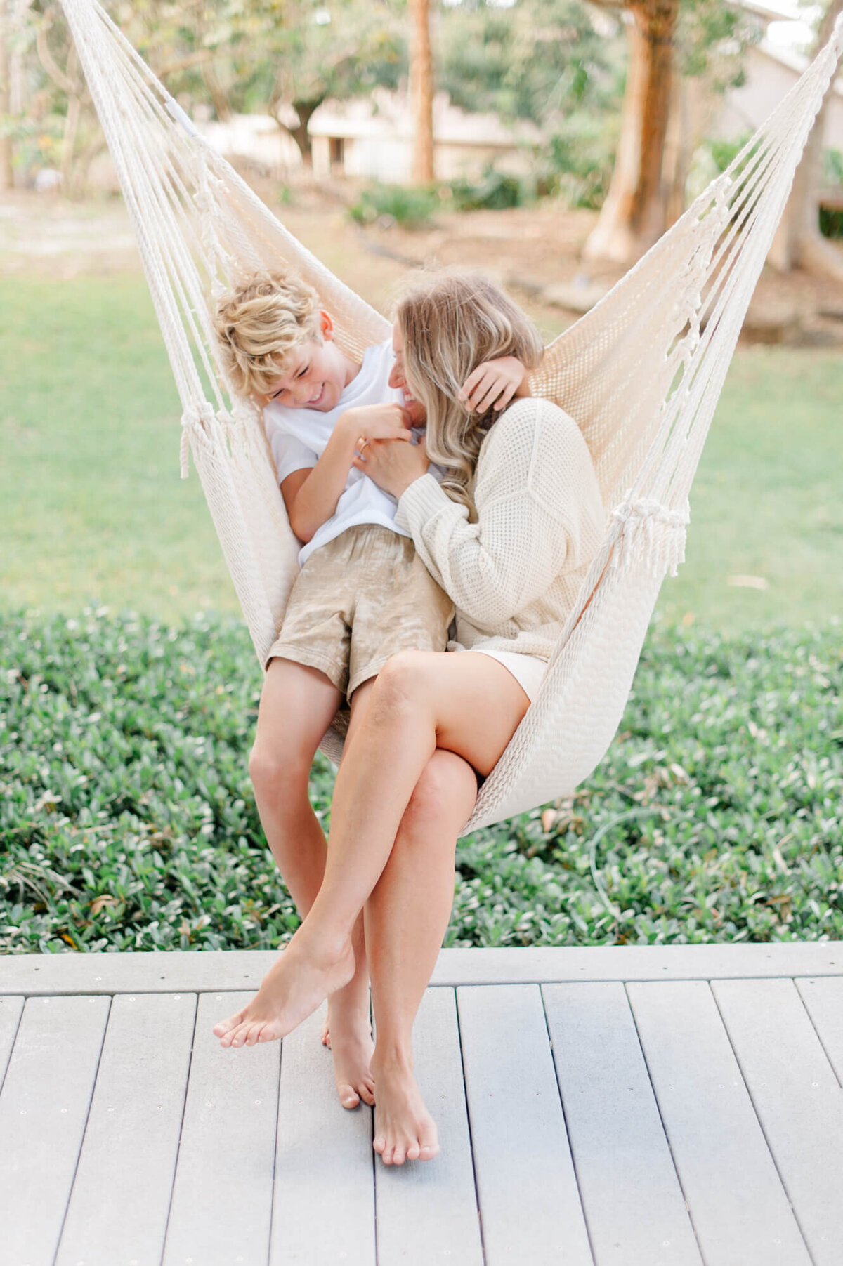 Mother and son sit in a hammock on the front porch while she tickles him during their family portraits