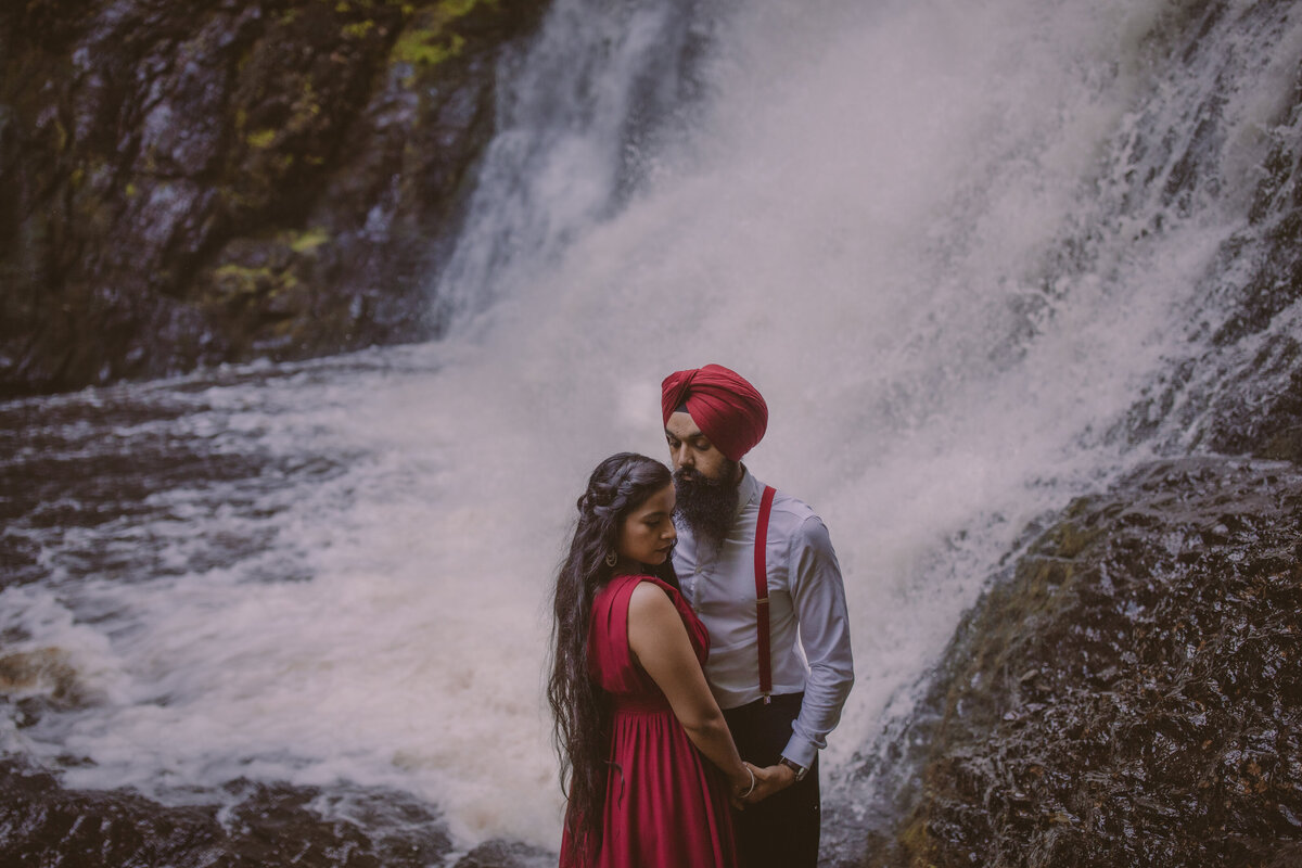 Sikh engagement couple in red outfits standing near the raymondskill waterfalls in the delaware water gap