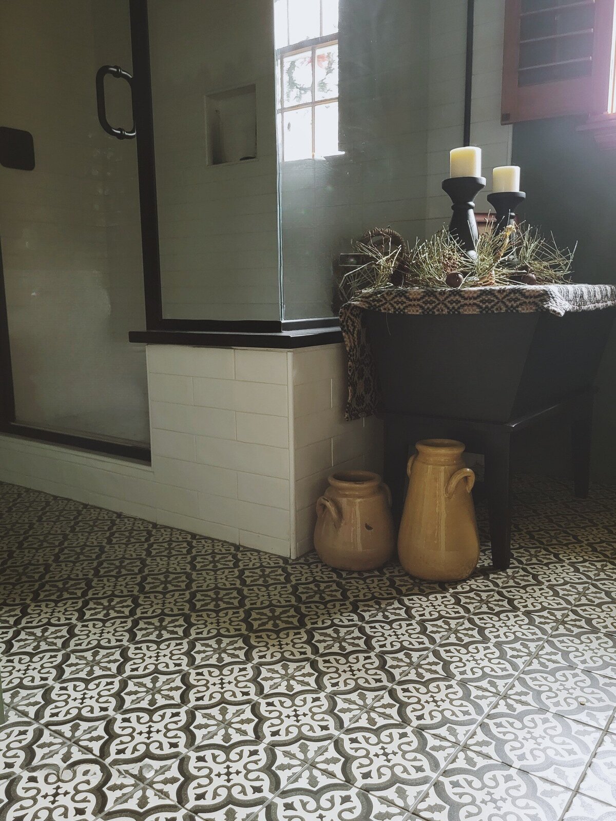 patterened tile bathroom floor with wooden cabinet, mustard pottery on floor alongside a white tiled walk in shower stall with glass doors in green painted bathroom