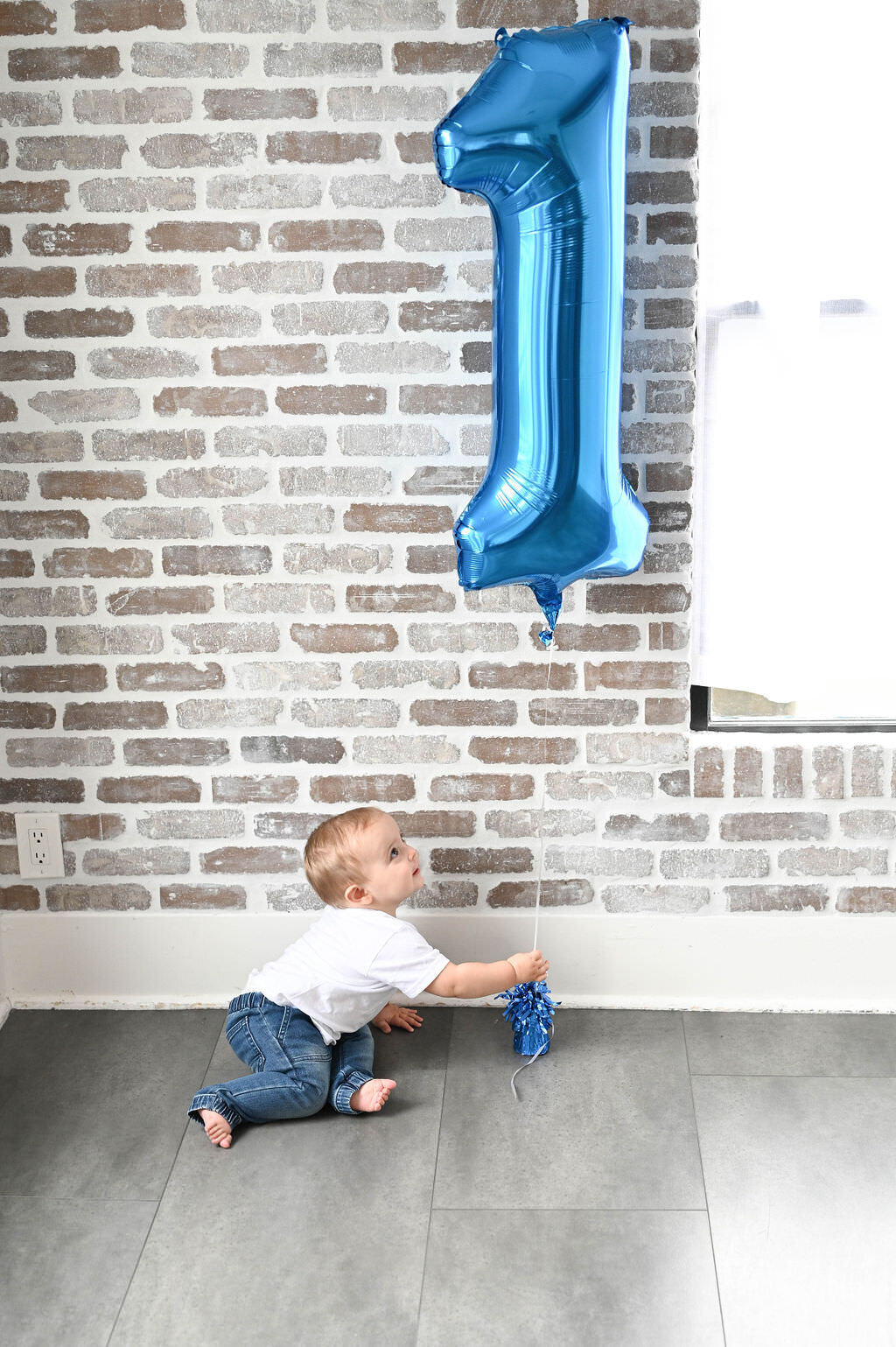 A small child on the ground playing with a one shaped balloon.