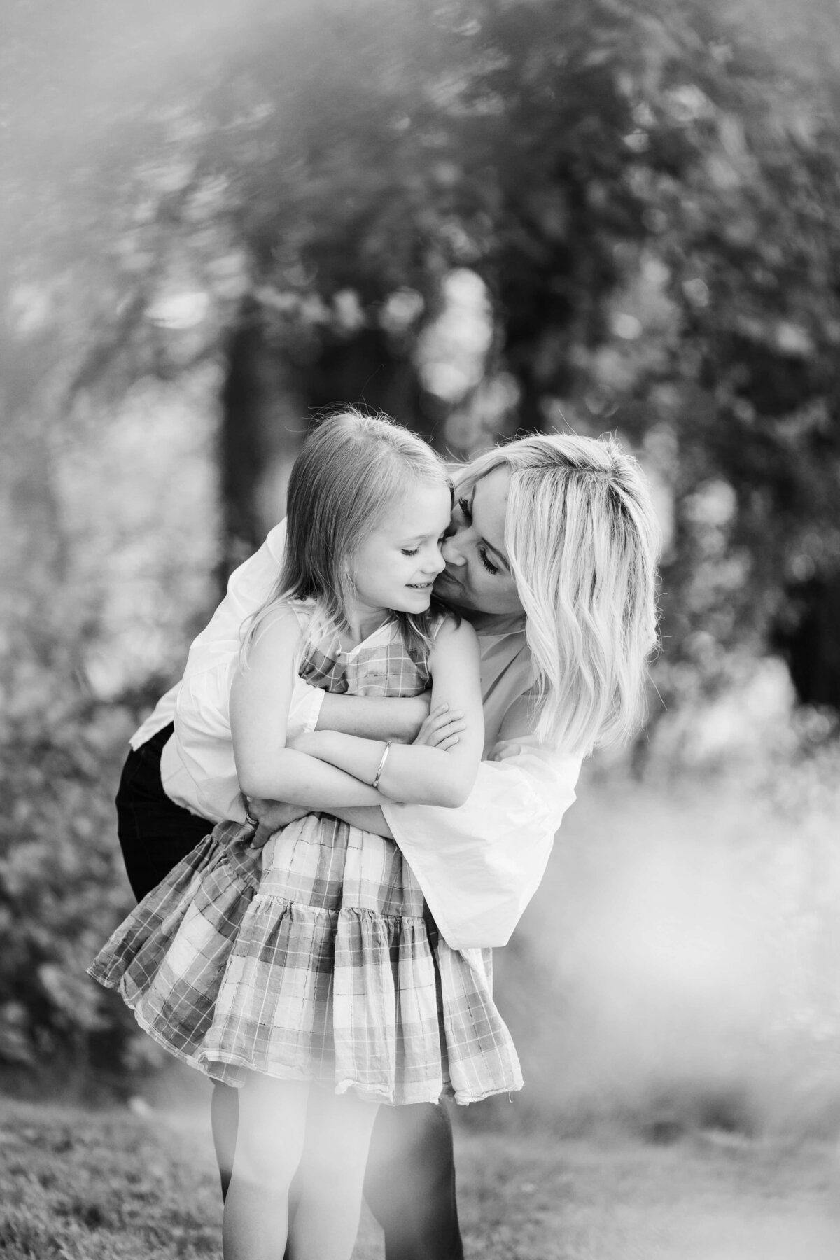 A Pittsburgh family photographer captures a tender moment of a mother affectionately kissing her young daughter on the forehead outdoors.