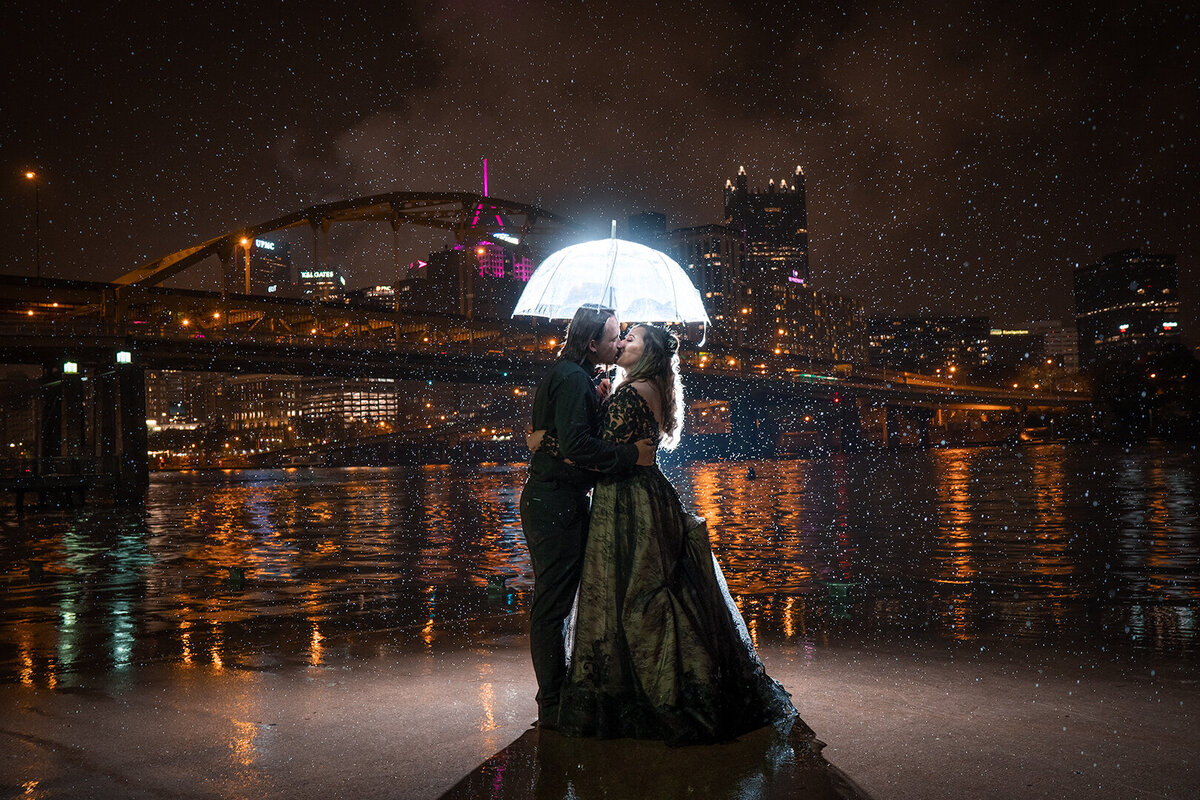 Bride and Groom stand under backlit umbrella in front of city skyline in Downtown Pittsburgh.