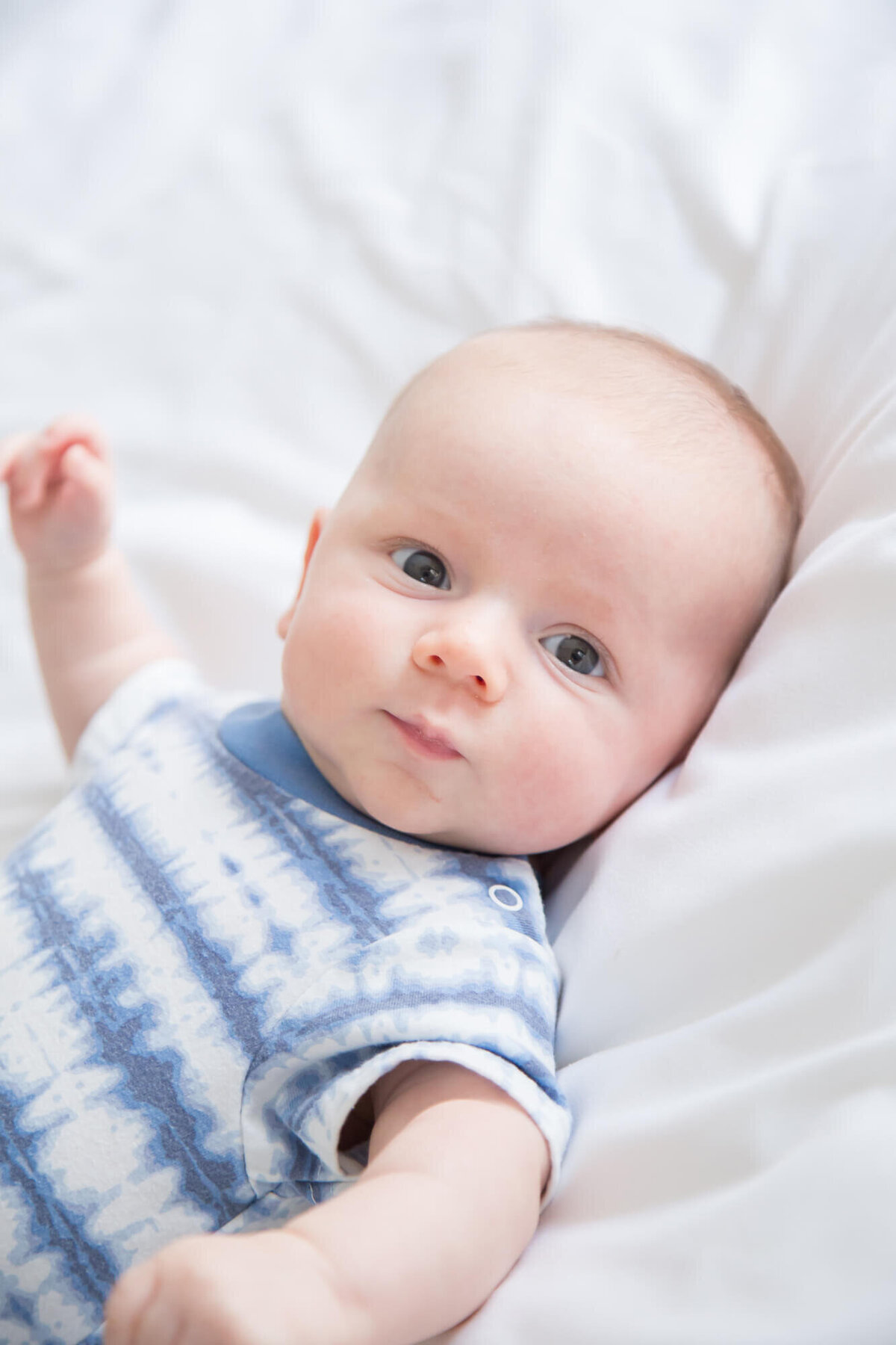 baby boy in white and blue tye dye shirt on a white bed