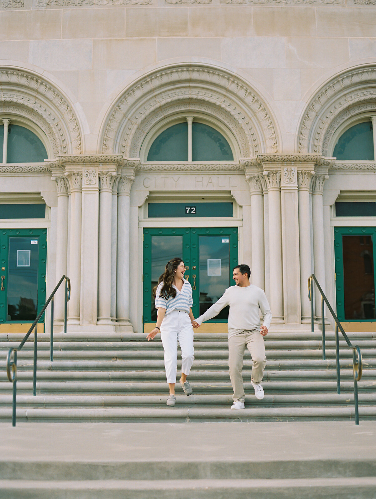 Man and woman holding hands and walking down stairs outside of a large stone building
