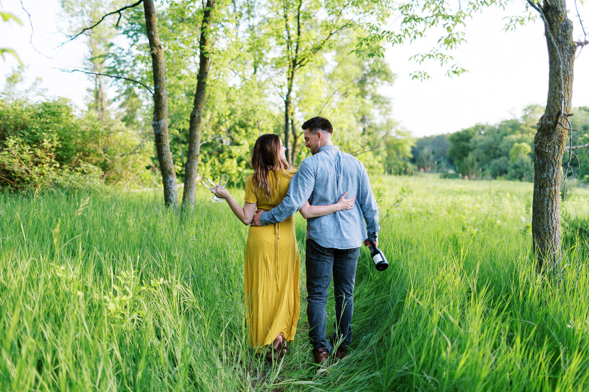 A couple walks arm in arm in Maple Grove, sharing a joyful moment with champagne in hand.