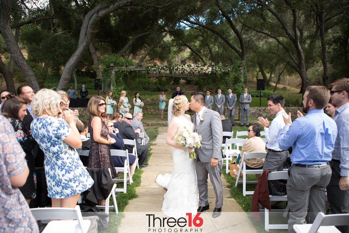 Bride and Groom stop on the aisle for another kiss as wedding guests applaud