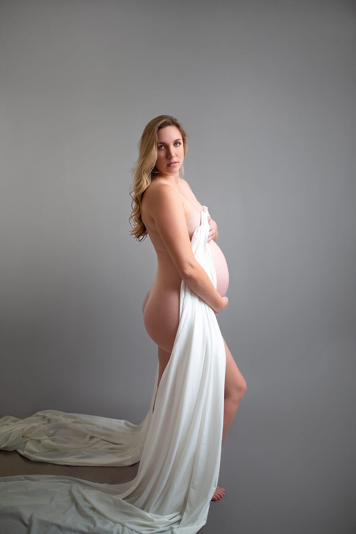 Blonde woman with fabric draped over pregnant body in simple and sexy maternity session 