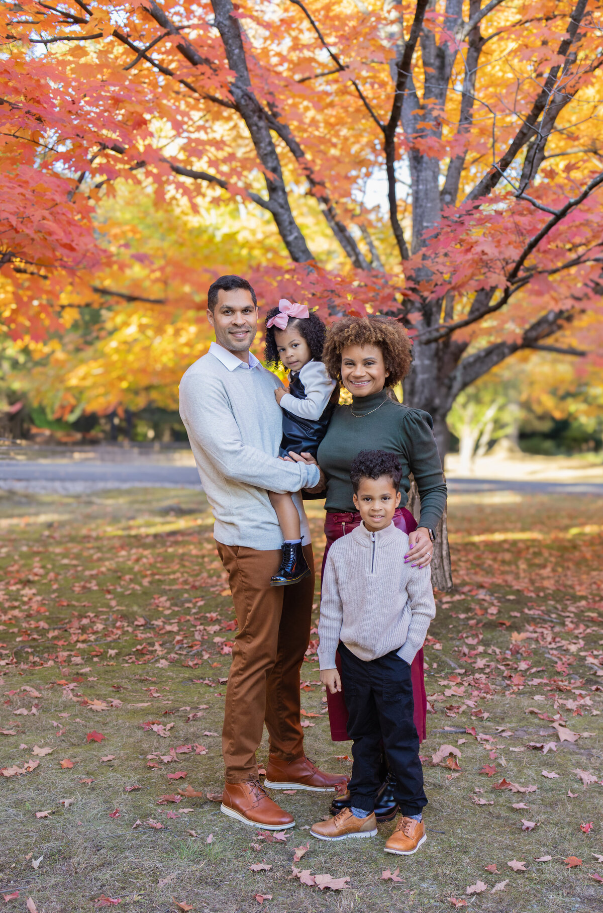 Autumn family portrait under bright orange maple trees with fallen leaves in Bergen County, NJ