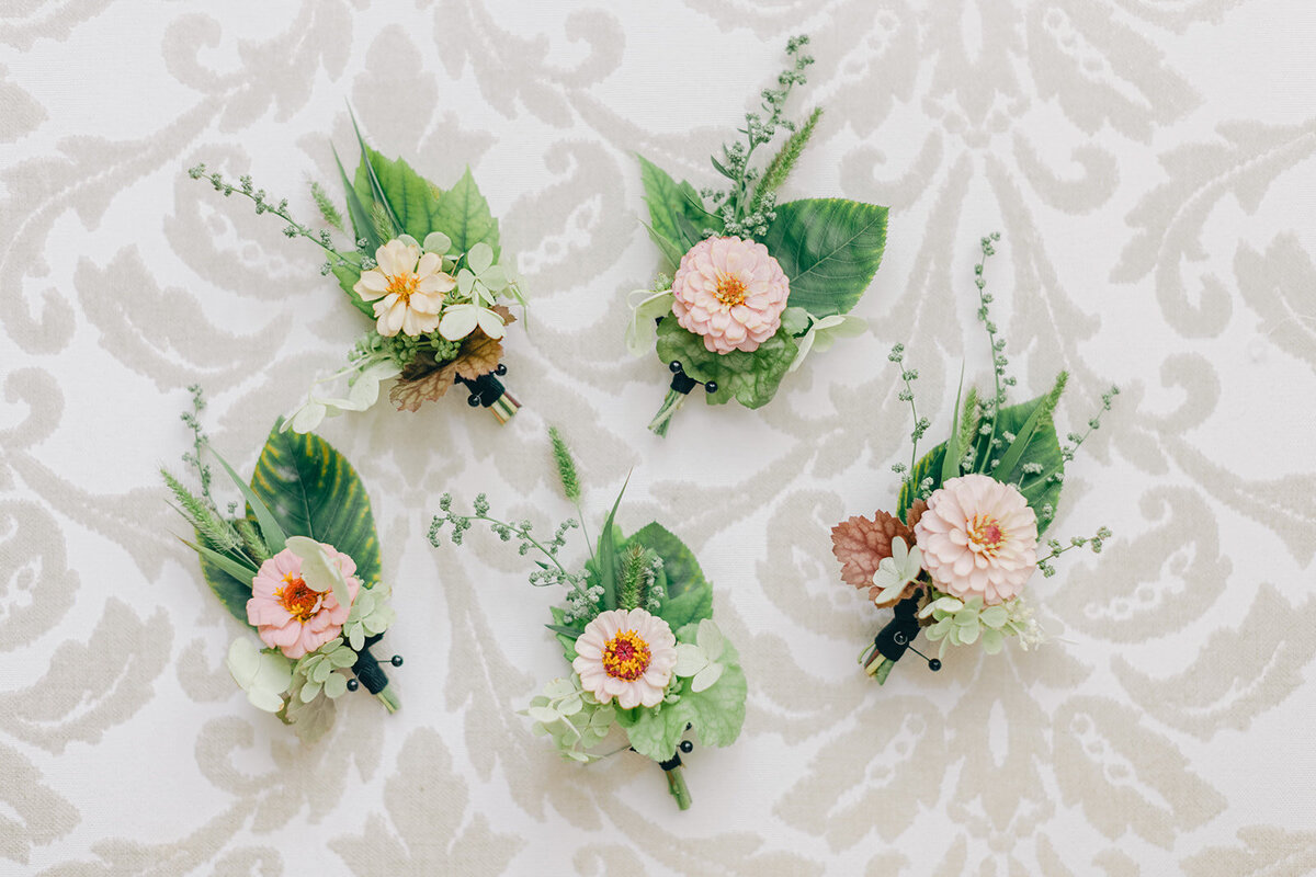 A set of pastel boutonnieres with lush greenery sit on a tablecloth at a Montreal wedding.