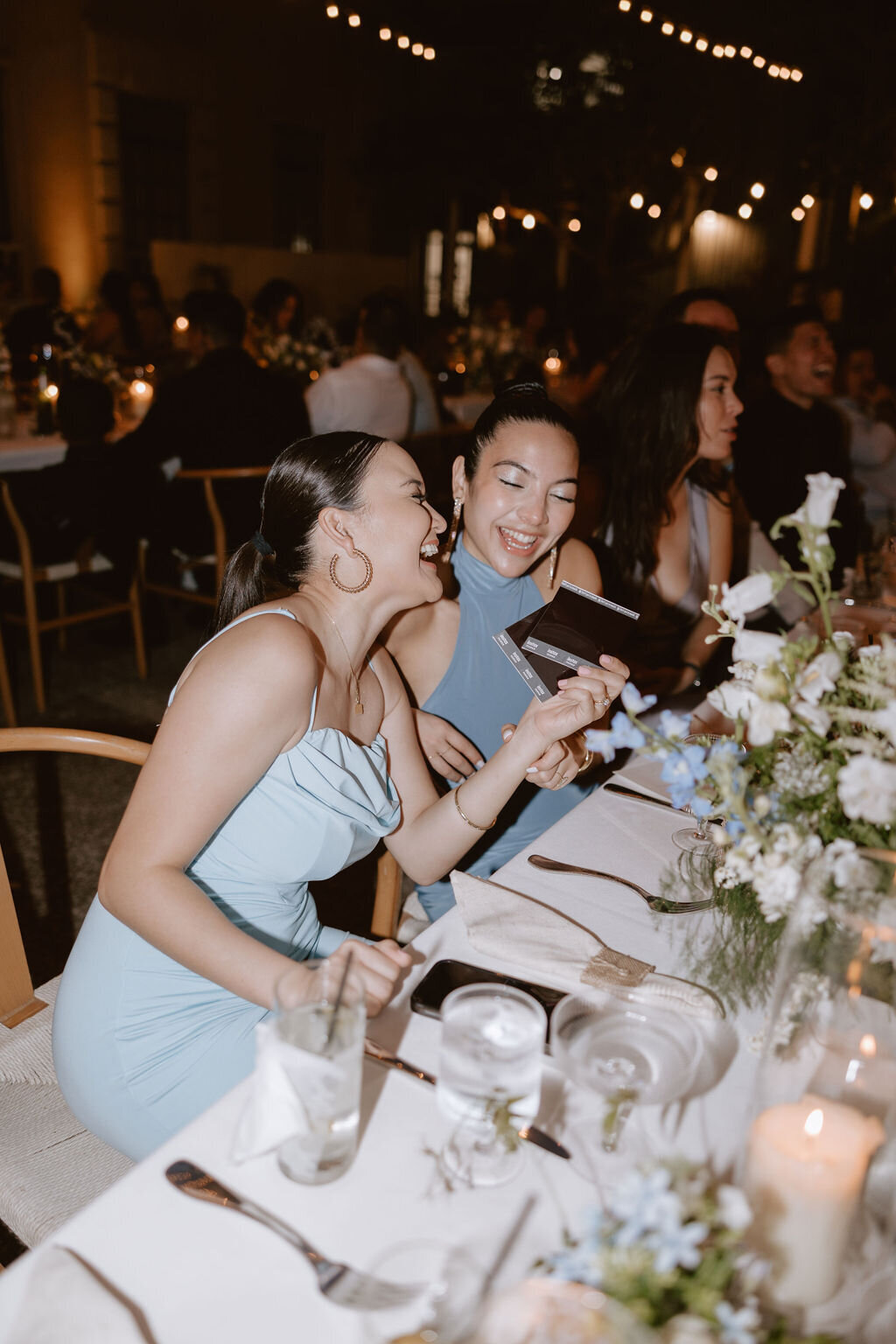 Two guests wearing baby blue looking at a poleroid photo and laughing while sitting at their table
