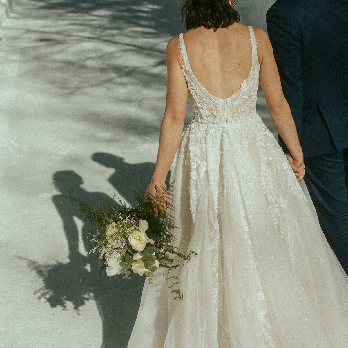 bridde and groom holding hands walking away from camera holding bouquet with their shadow in front of them