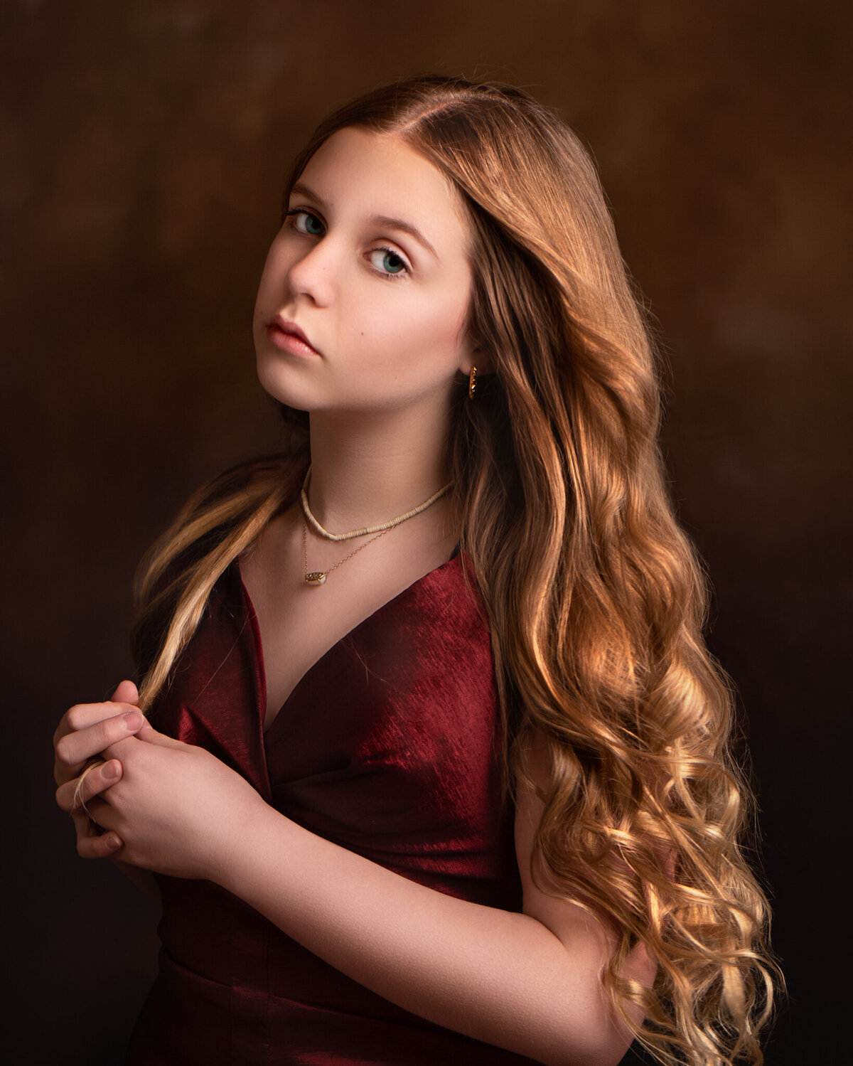 Fine art portrait of a young girl with flowing golden hair in a sophisticated pose, captured against a rich brown backdrop. Captured in Overland Park, Kansas, this artistic and polished setup is perfect for timeless child photography