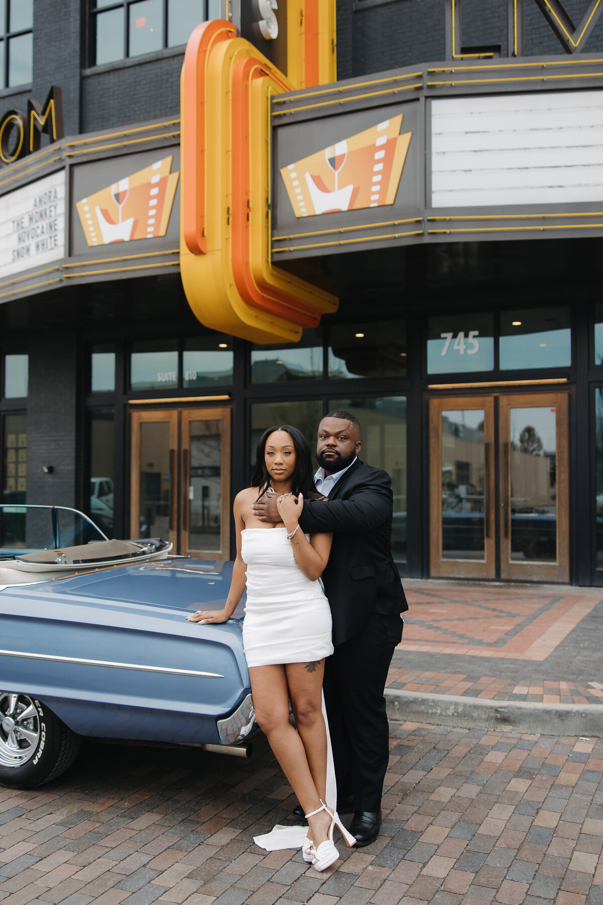 This photo shows a newly engaged couple standing in front of a classic blue car. They are standing under a marquee sign in Bottleworks District in Indianapolis, Indiana.
