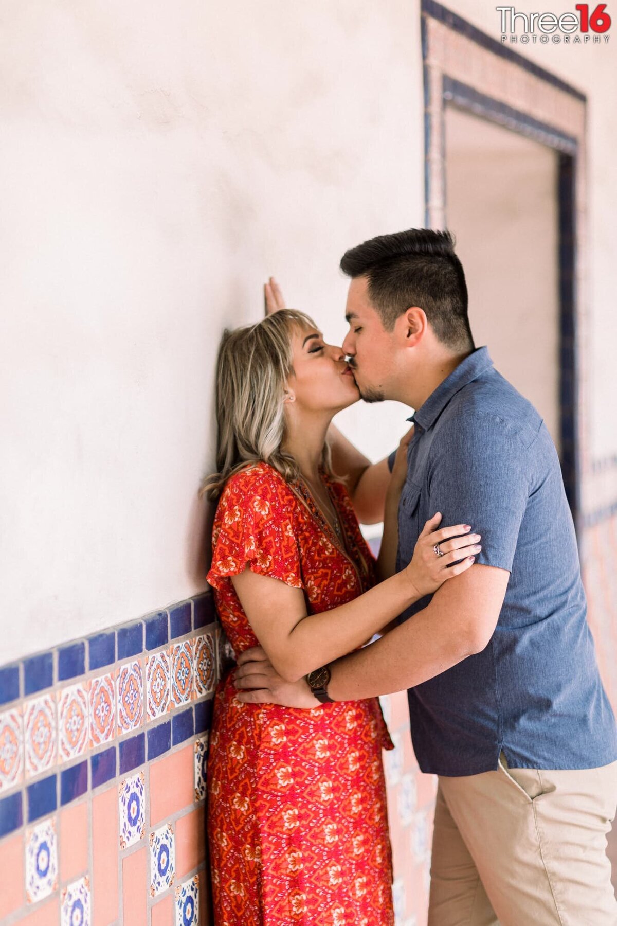 Engaged couple share a kiss while leaning against a Santa Ana Train Station wall
