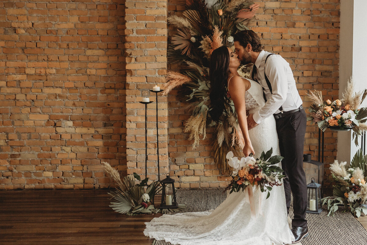 Couple kissing at their boho inspired wedding, The Garret, historical and sophisticated, Calgary, Alberta wedding venue, featured on the Brontë Bride Vendor Guide.