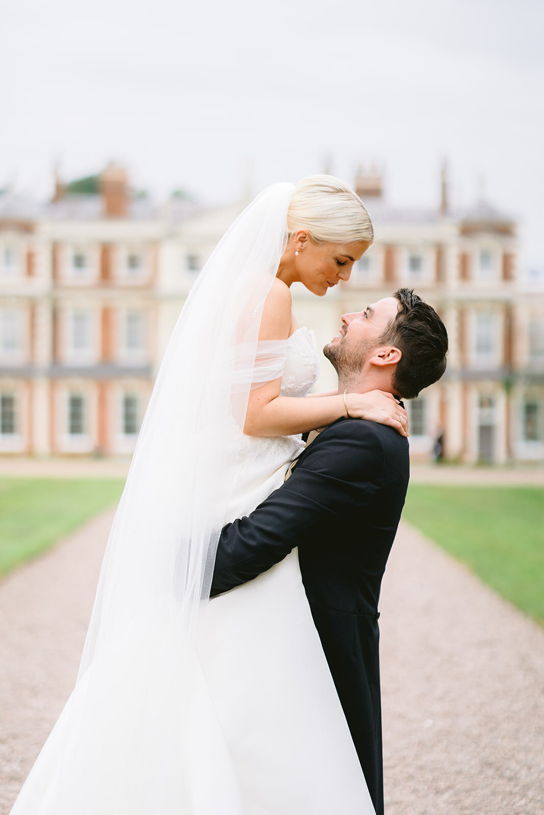 hawkstone hall wedding photo of groom holding bride in the air with venue in the background