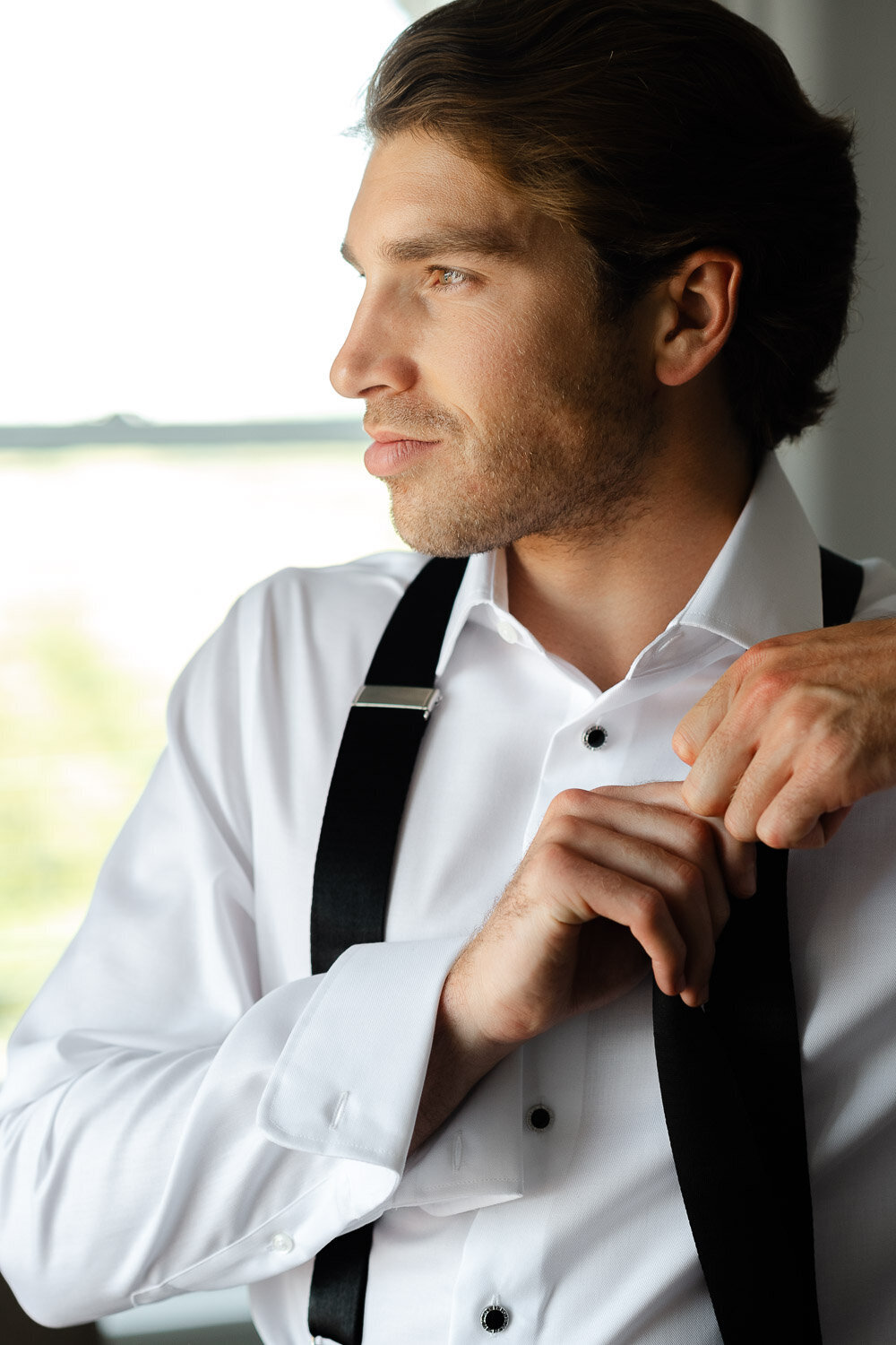 groom adjusting suspenders by window