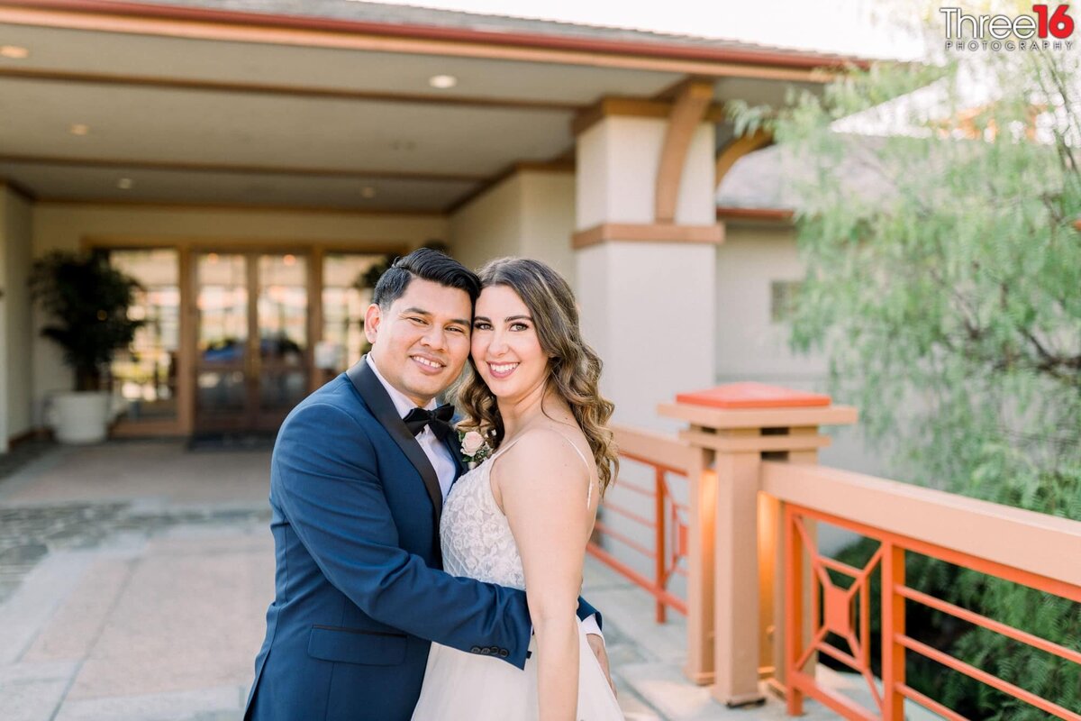 Groom holds his Bride as they pose for a photo on the bridge that leads to the entry of the Coto de Caza Golf & Racquet Club