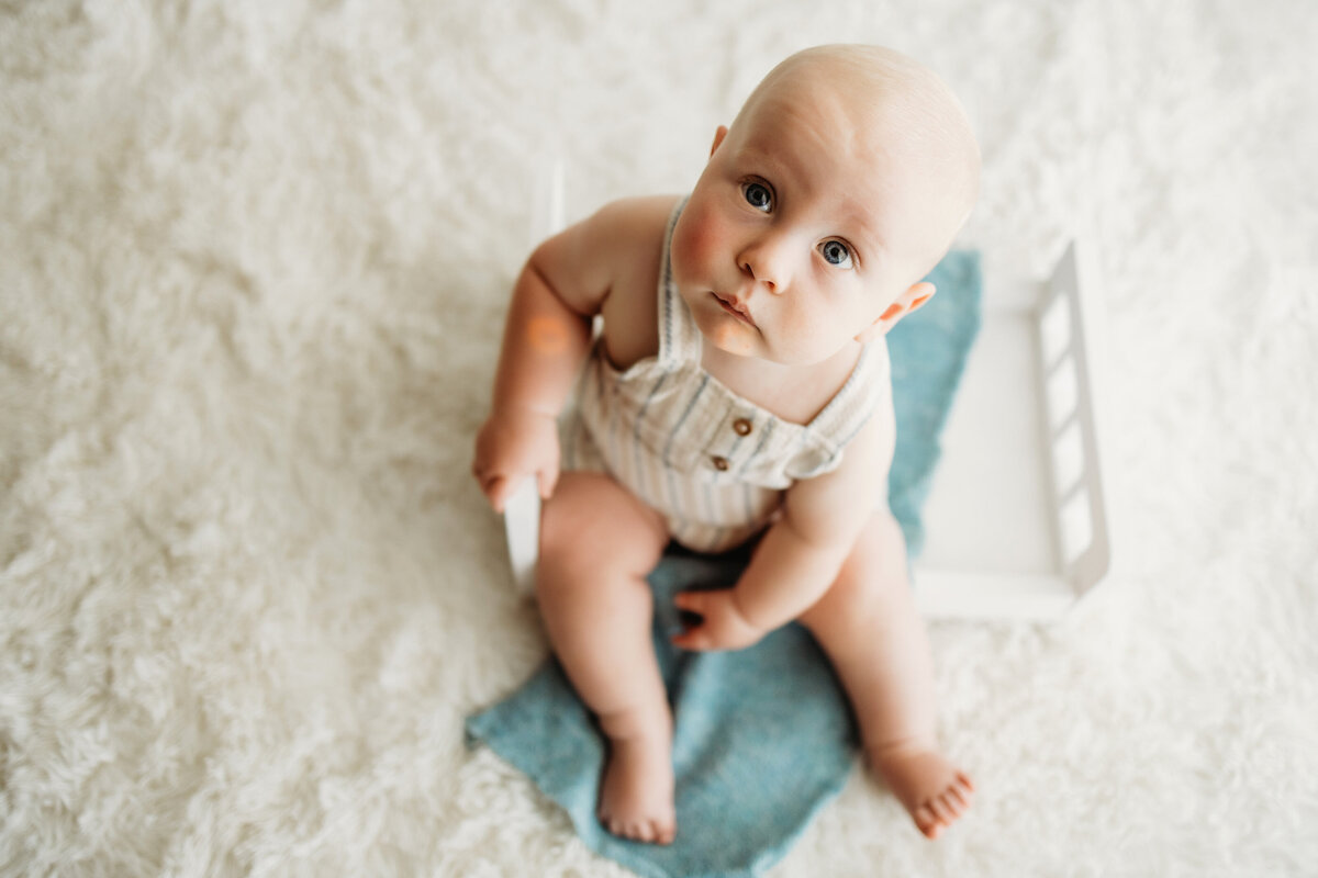 Infant six month old baby boy looking up at the camera during his milestone sitter session in Denver.
