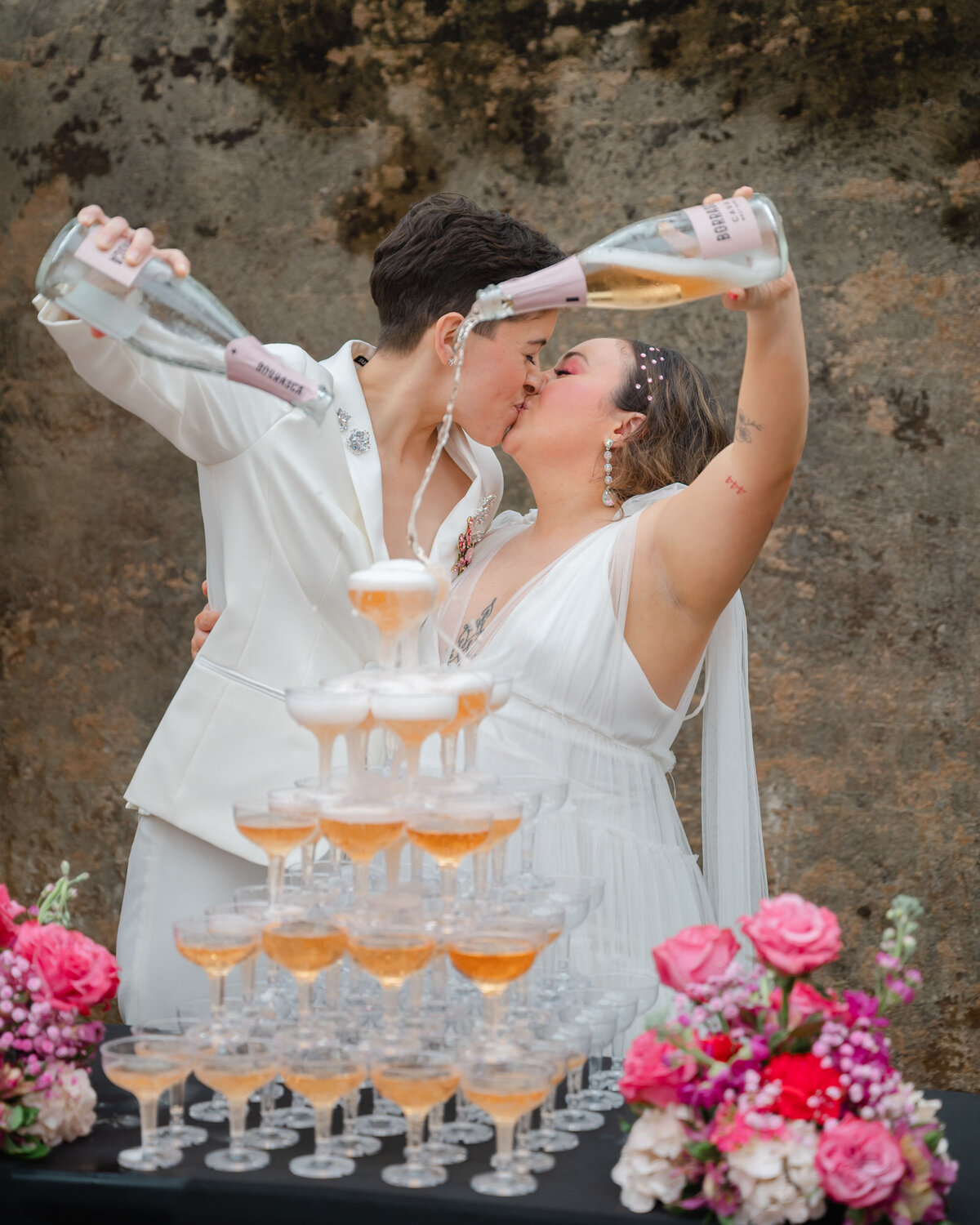 Two brides kissing while pouring champagne in champagne tower