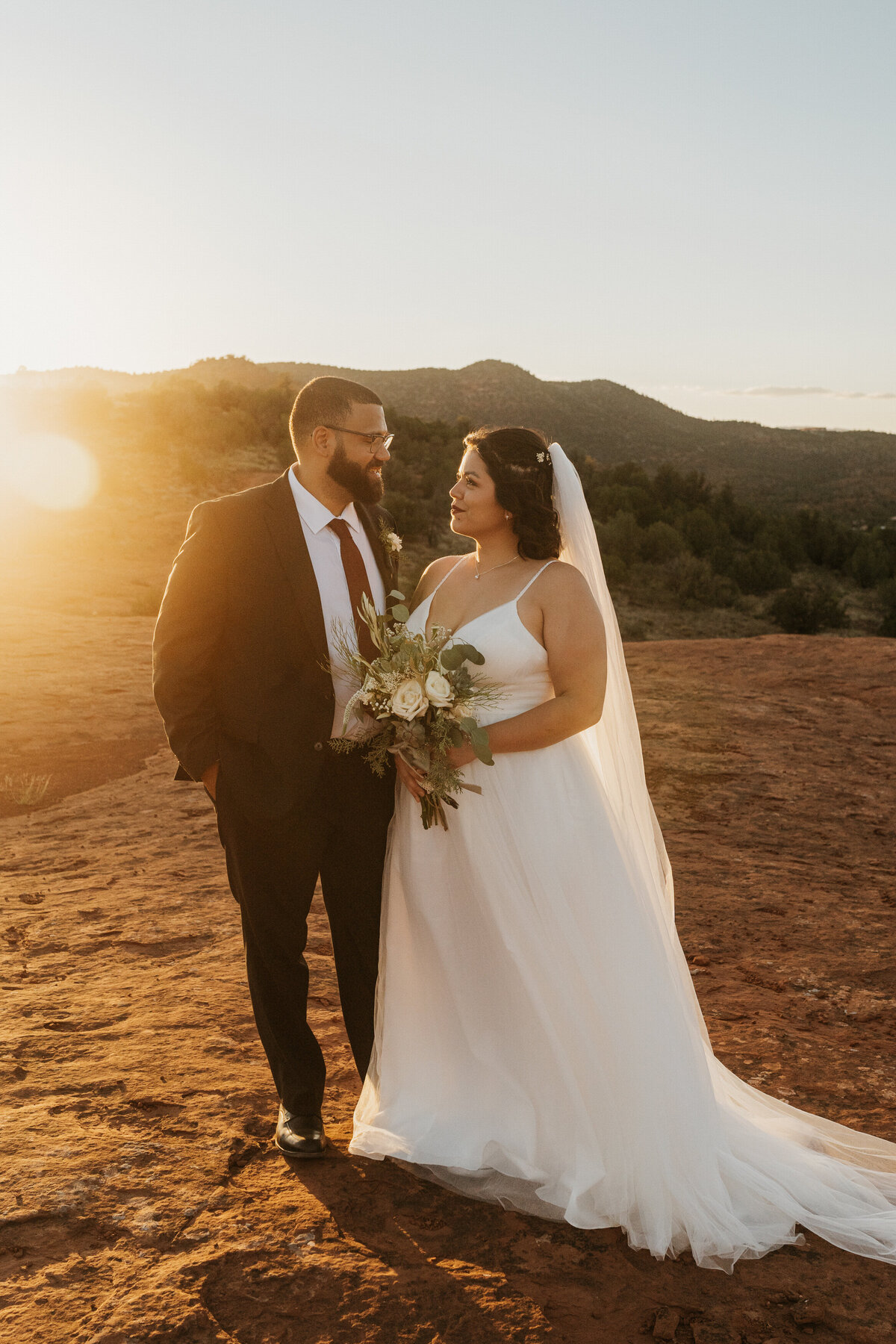 A wedding couple standing close together and smiling at each other at sunset 