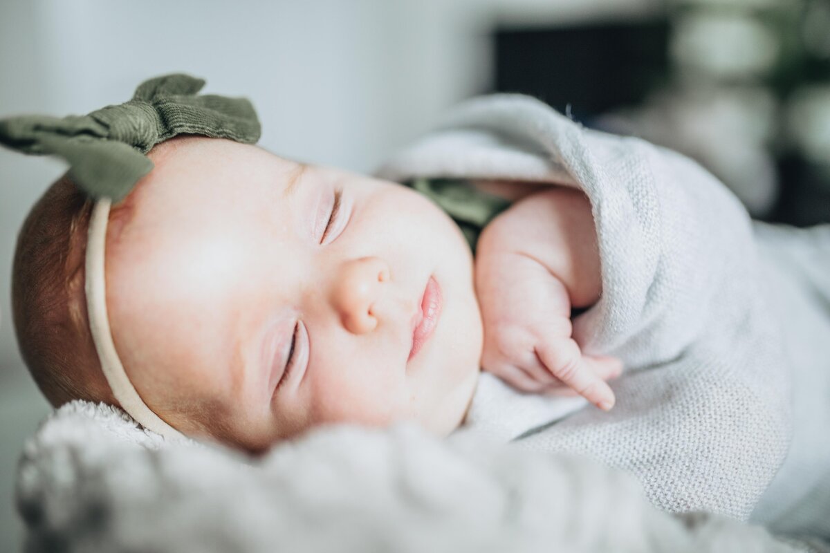 newborn baby girl sleeping in a light grey swaddle wearing a green bow on her head photographed by Idaho Falls newborn photographer