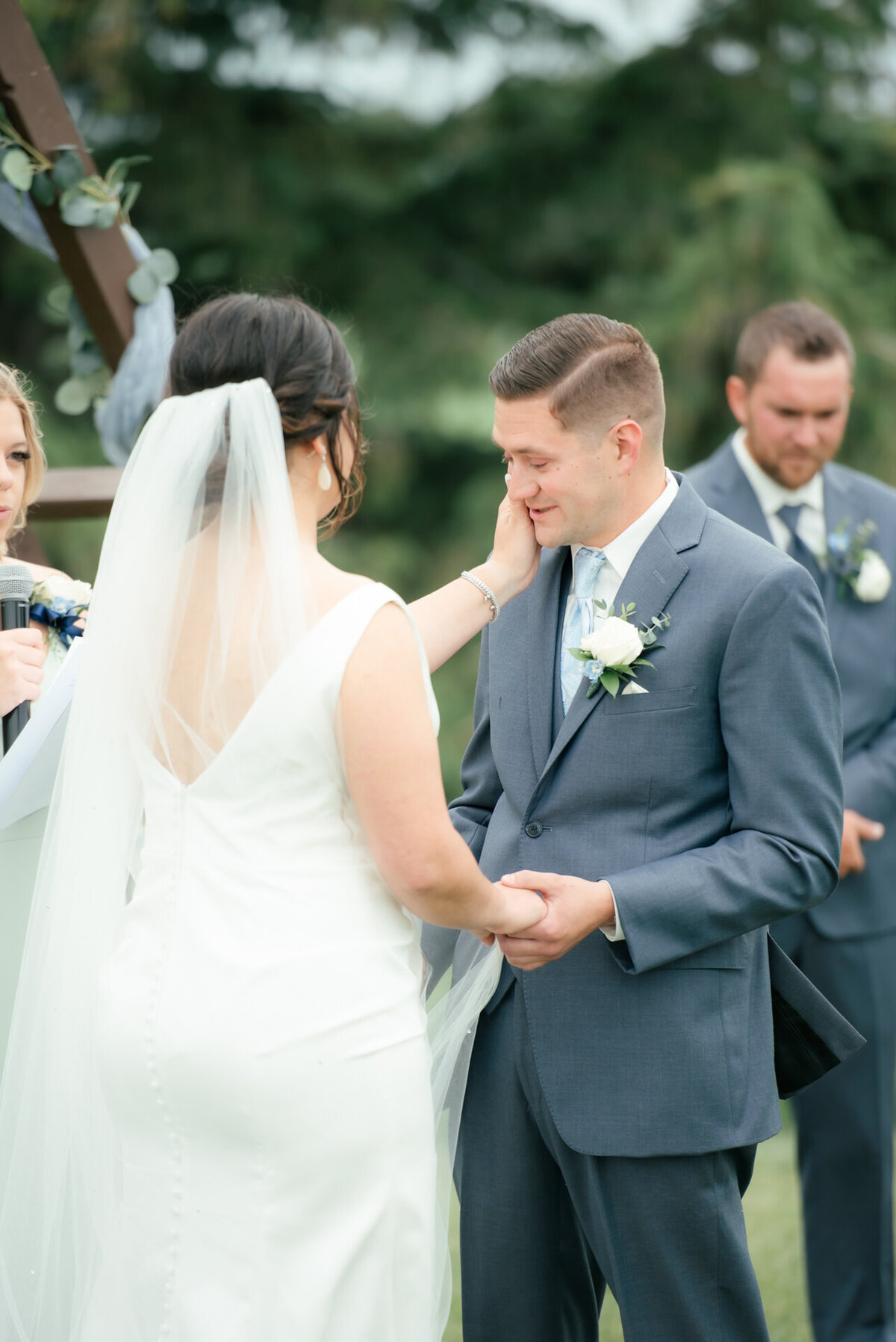 bride wipes a tear from the groom's face during wedding ceremony