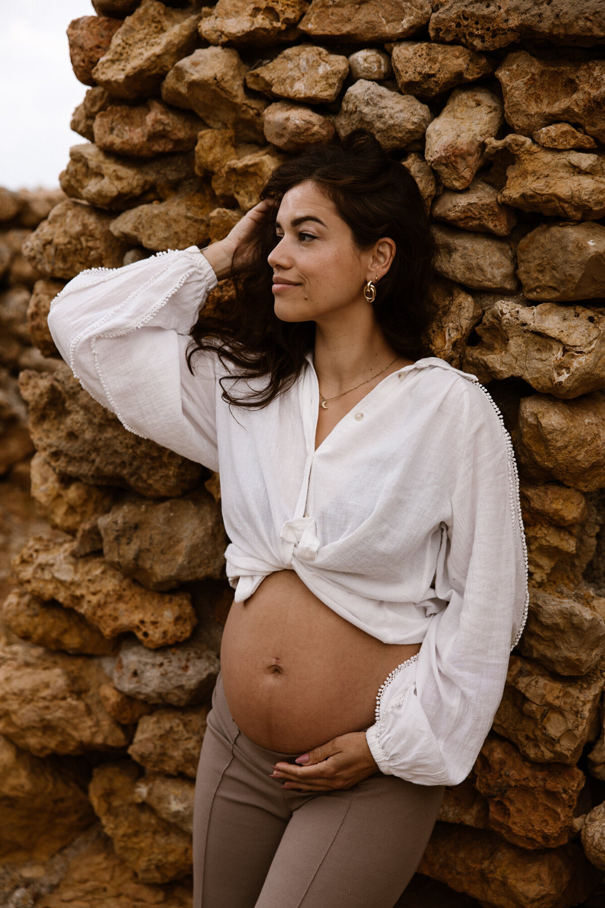 Pregnant woman going through her hair while posing in front of a rock wall on Ibiza during a pregnancy photoshoot