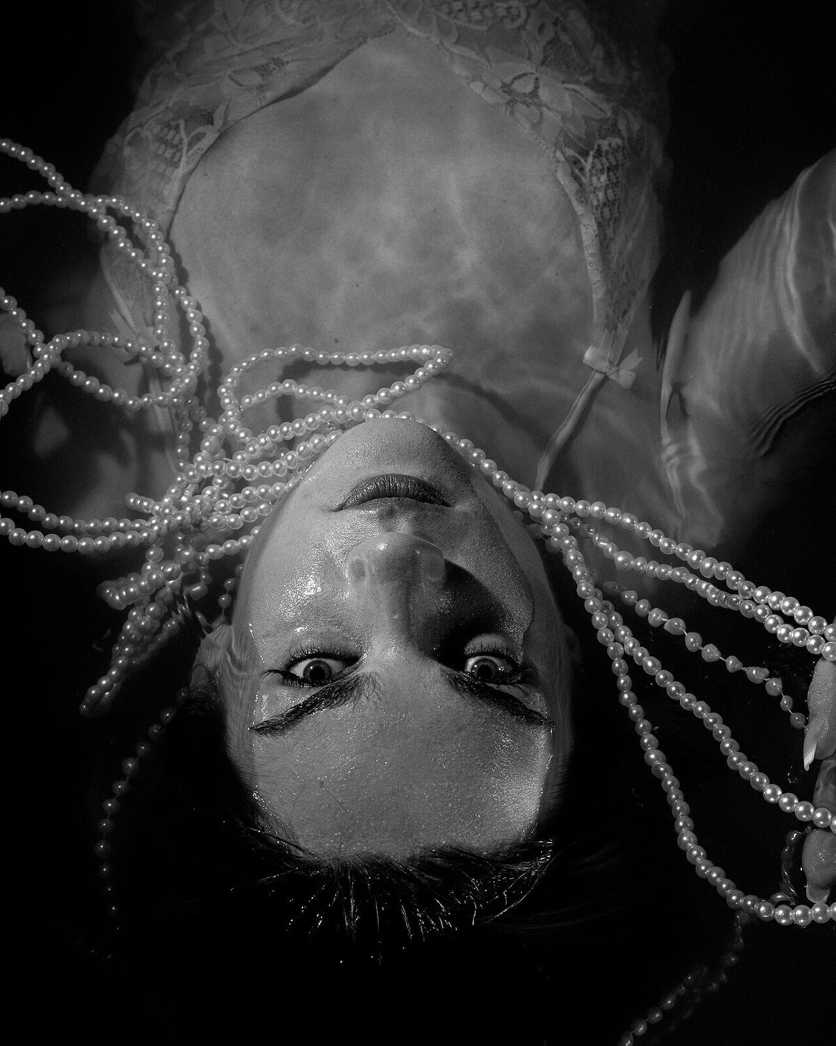 Intimate boudoir photo shoot, a bride lays in a bath of water. She wears a slip and is draped in pearls.