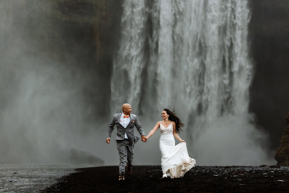 married couple is laughing and hugging in fron of the Skogafoss waterfall in Iceland