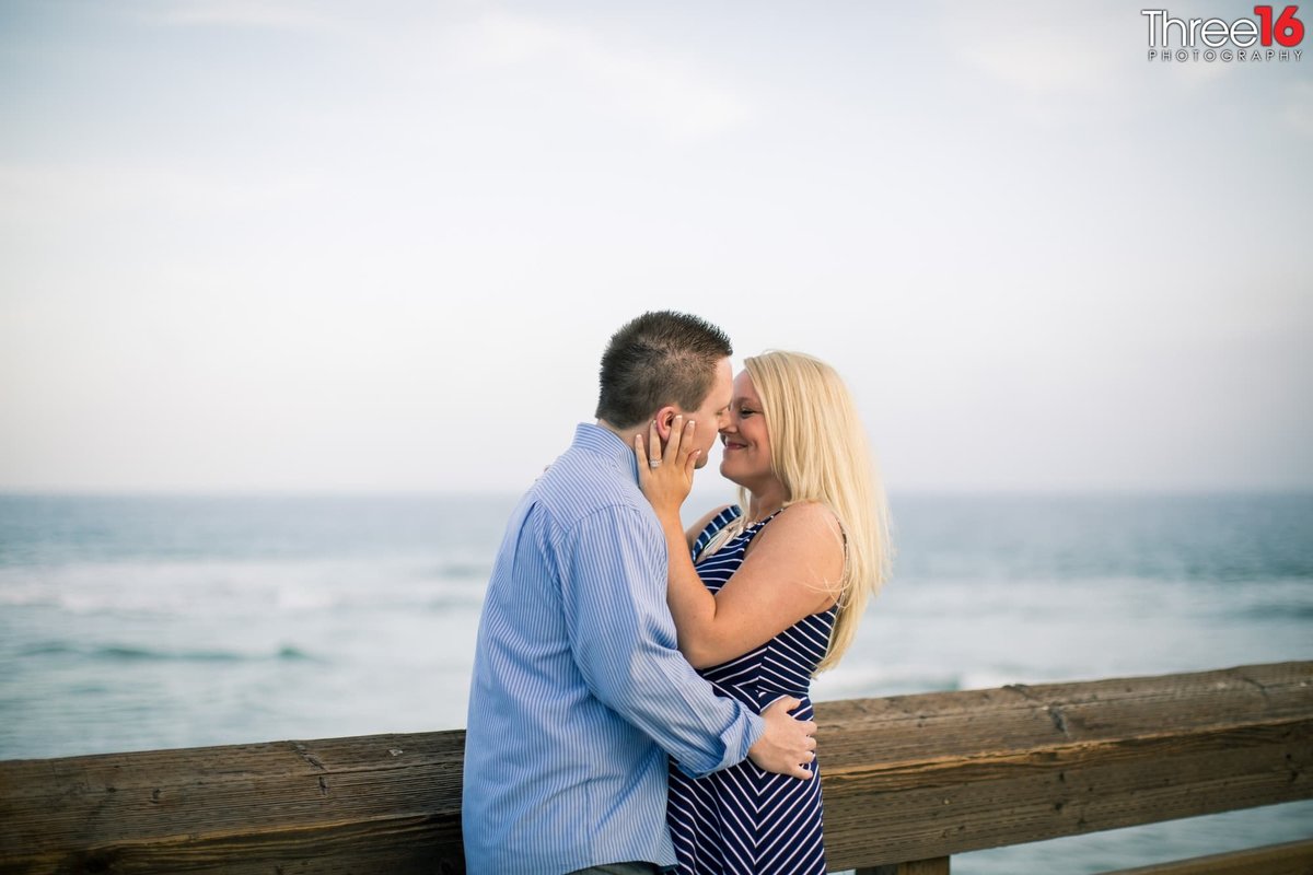 Tender moment for engaged couple along the railing on the Newport Beach Pier