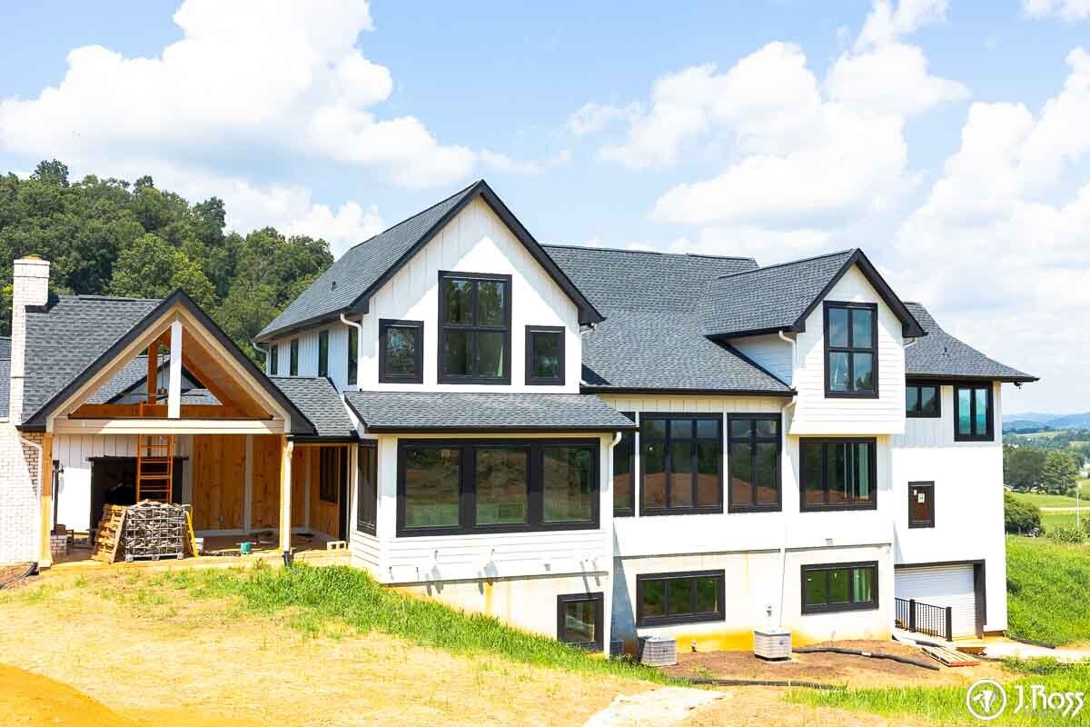 Wide angle view of the large white modern farmhouse under construction, showing the multi-gabled roofline and black window frames, a project for home outside painting, Kingsport, Tennessee.