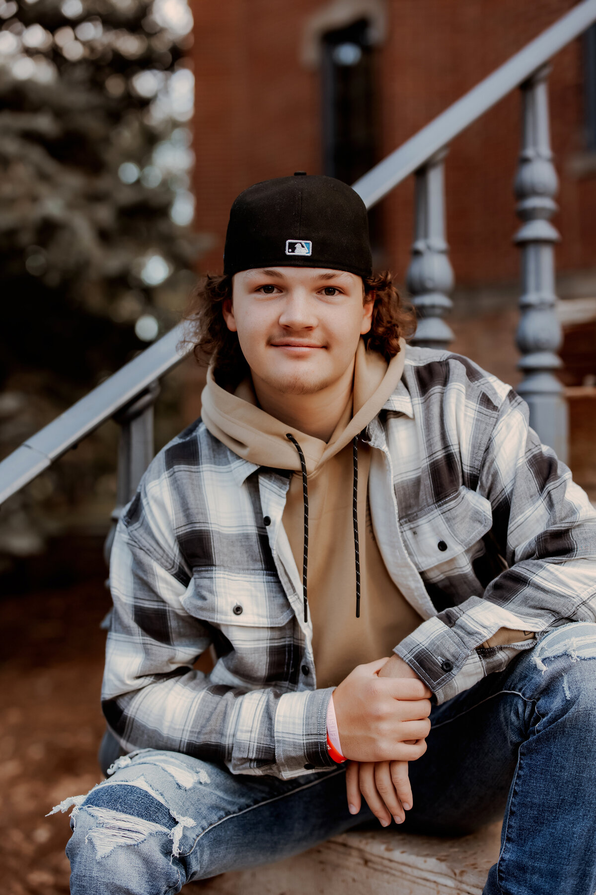 Senior boy in a plaid and tan shirt leaning against a stair rail in Boulder