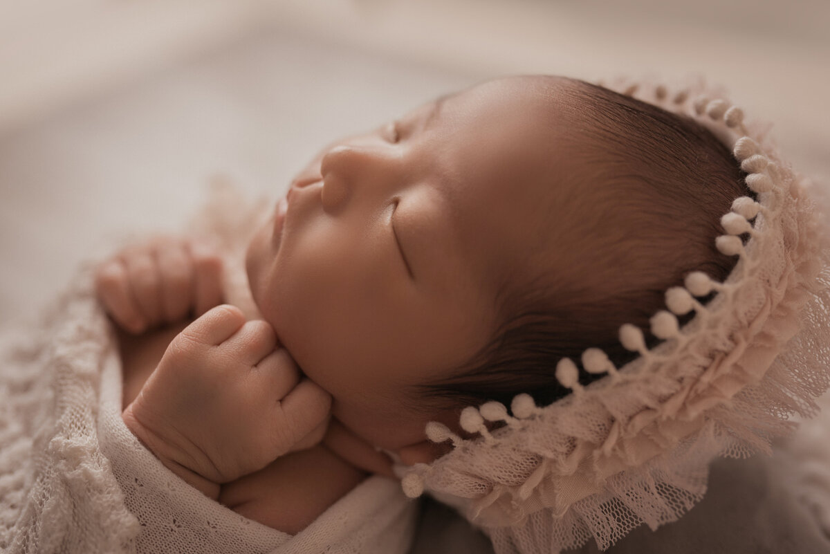 baby girl at newborn photo  shoot in marietta ga asleep and wrapped in white lace with  cream and light pink bonnet on