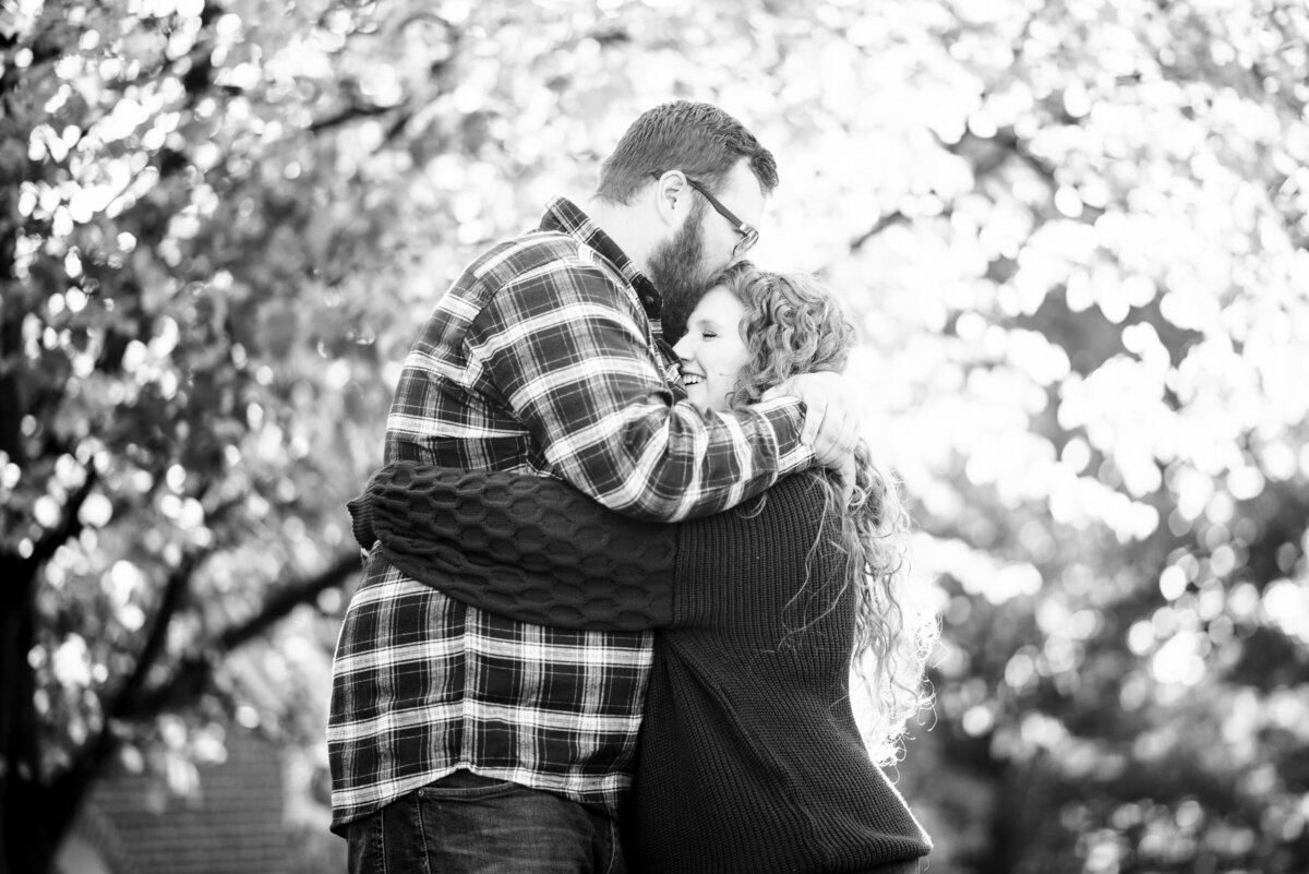 Black-and-white-photograph-of-couple-embracing-and-laughing-in-a-hug-outdoors-as-part-of-their-engagement-session-in-Winston-Salem-NC